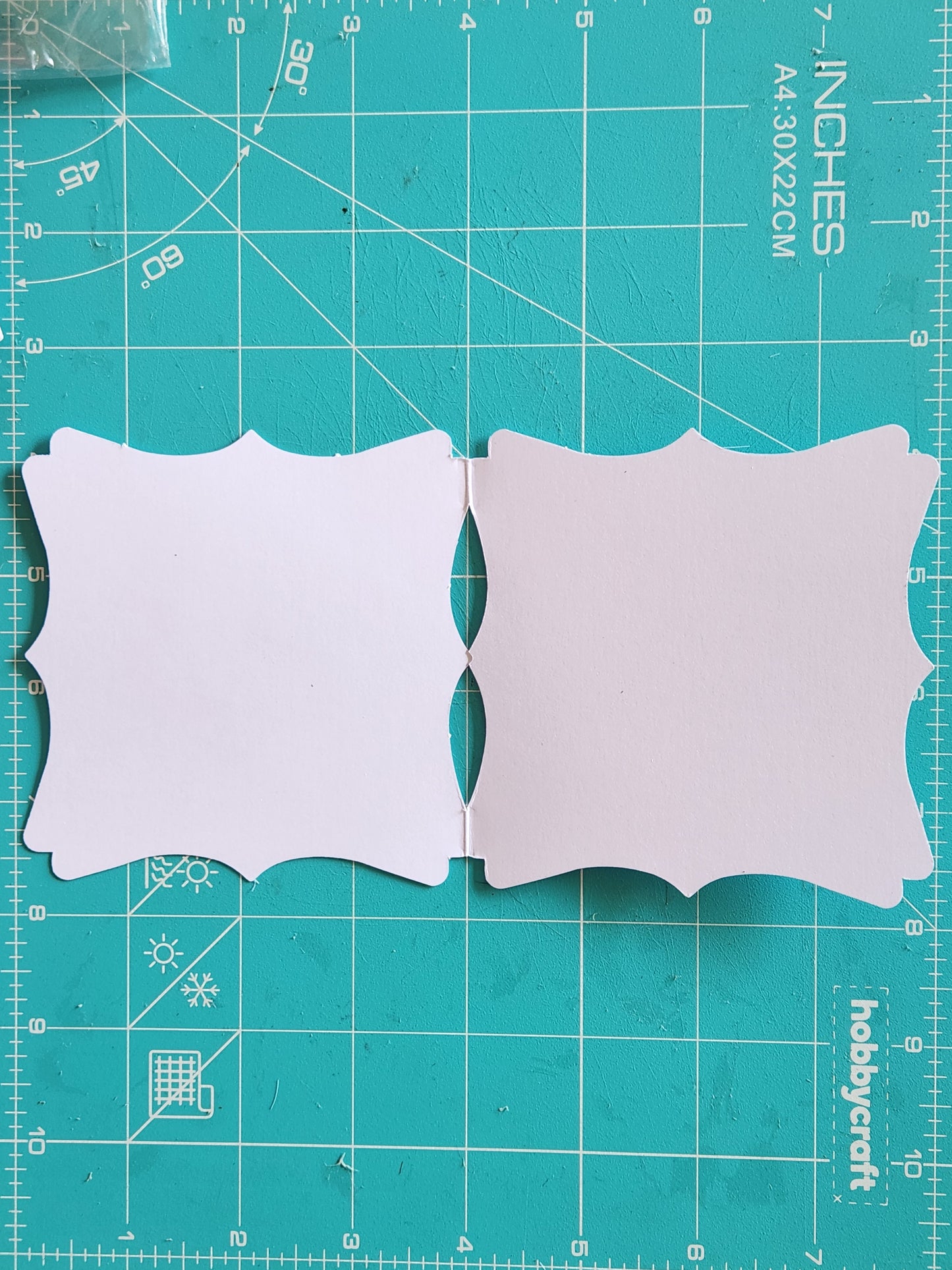 The blank inside of a white paper card with decorative edges on a teal cutting mat.